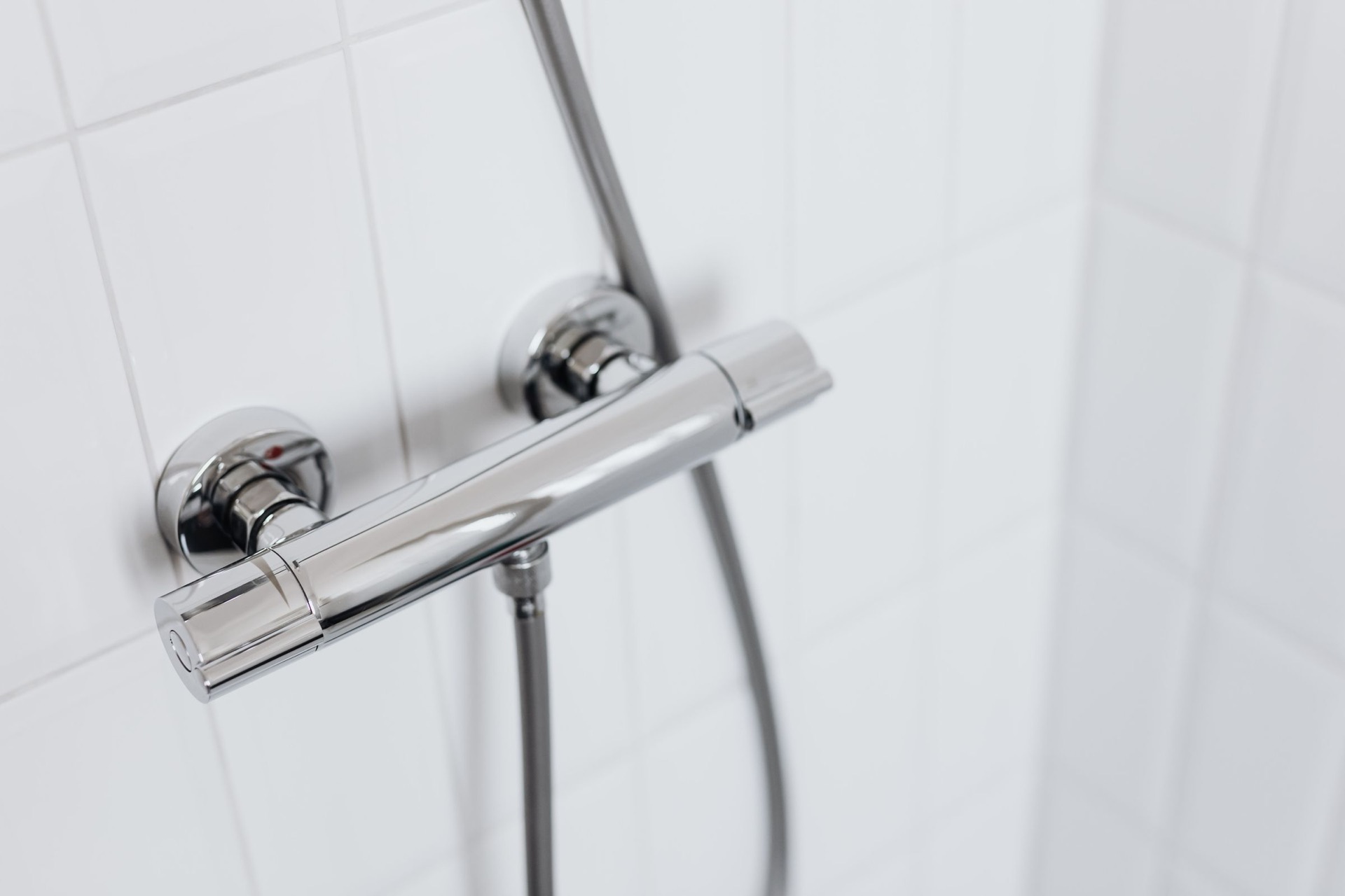 Een glanzende thermostaatkraan en een doucheslang tegen witte tegels