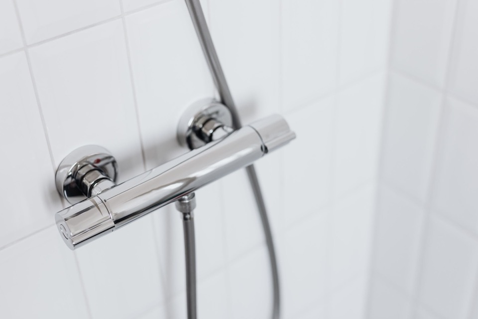 Een glanzende thermostaatkraan en een doucheslang tegen witte tegels