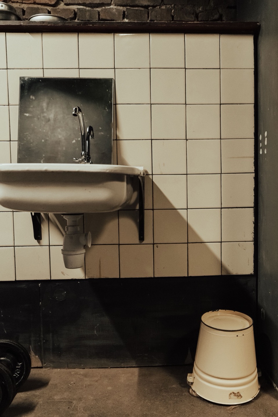 Een wastafel met een emmer tegen een wit betegelde muur